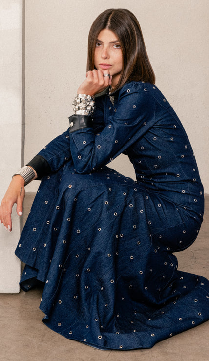 A woman modeling a dark navy blue long-sleeve dress with small white embroidered dots and black collar/cuff accents, posed against a light gray studio background.
