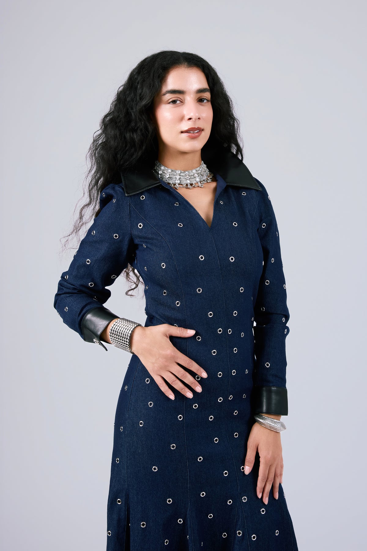 A woman modeling a dark navy blue long-sleeve dress with small white embroidered dots and black collar/cuff accents, posed against a light gray studio background.