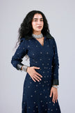 A woman modeling a dark navy blue long-sleeve dress with small white embroidered dots and black collar/cuff accents, posed against a light gray studio background.