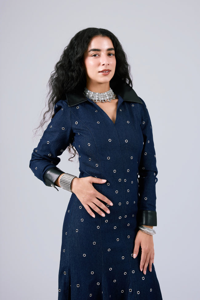 A woman modeling a dark navy blue long-sleeve dress with small white embroidered dots and black collar/cuff accents, posed against a light gray studio background.
